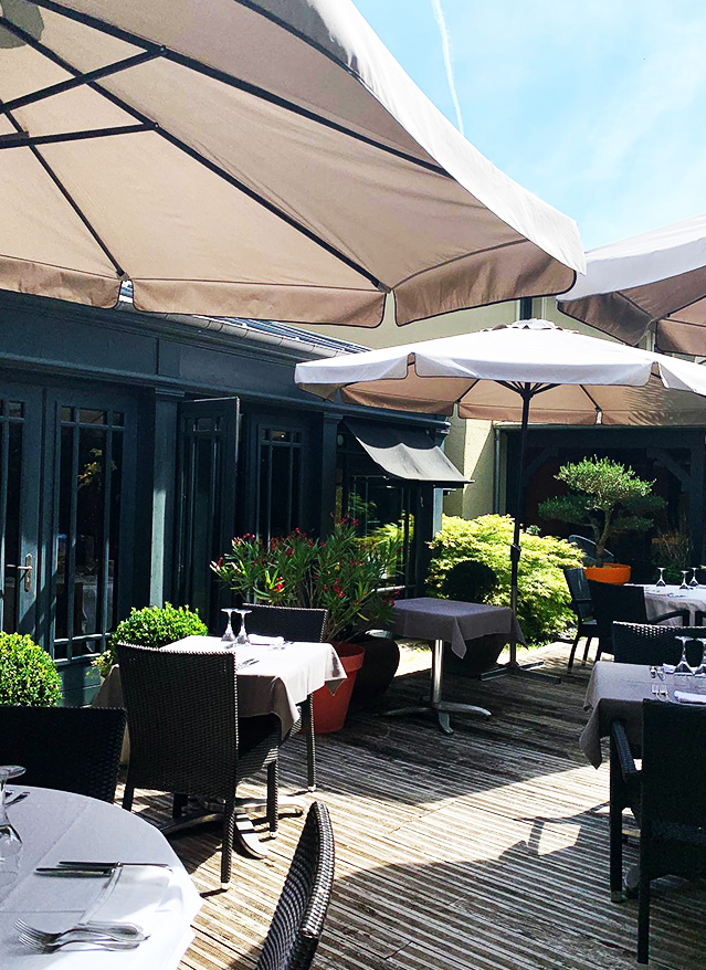 Coin salon extérieur avec canapé et tables sur la terrasse ombragée du restaurant